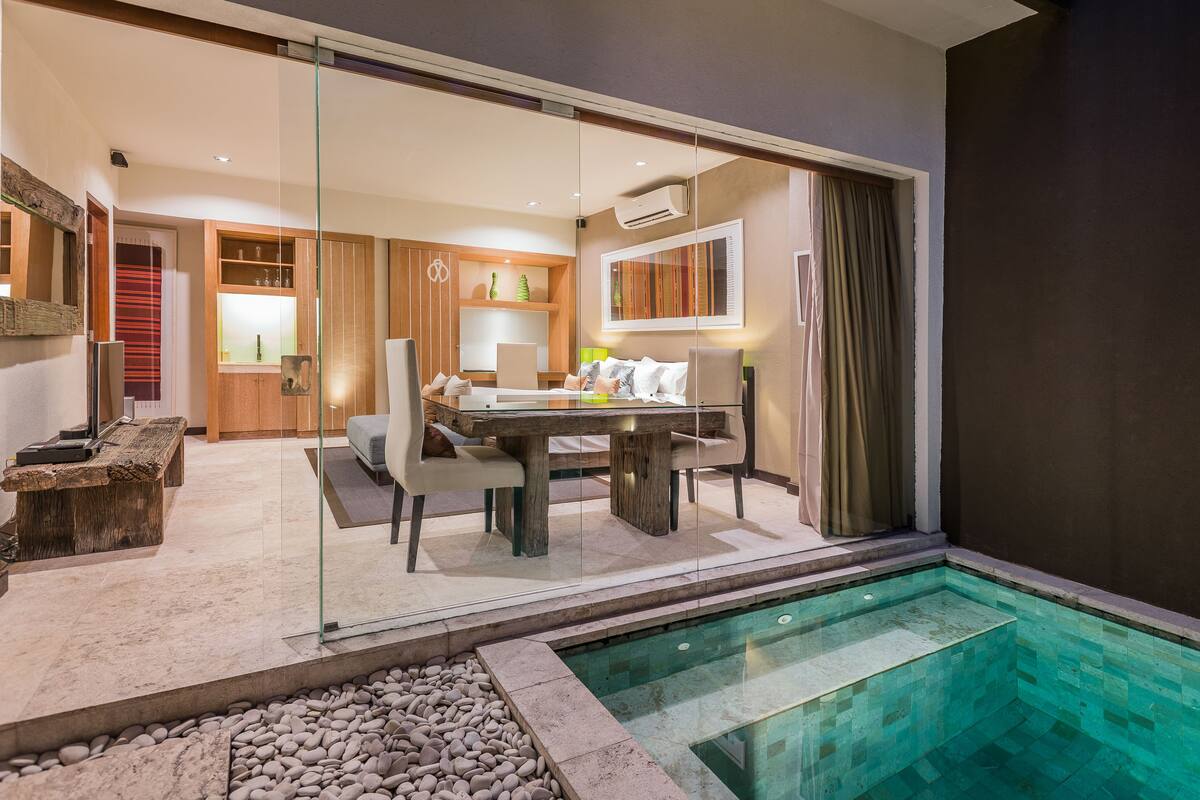A modern hotel room with a glass wall, a dining area, and a small pool.