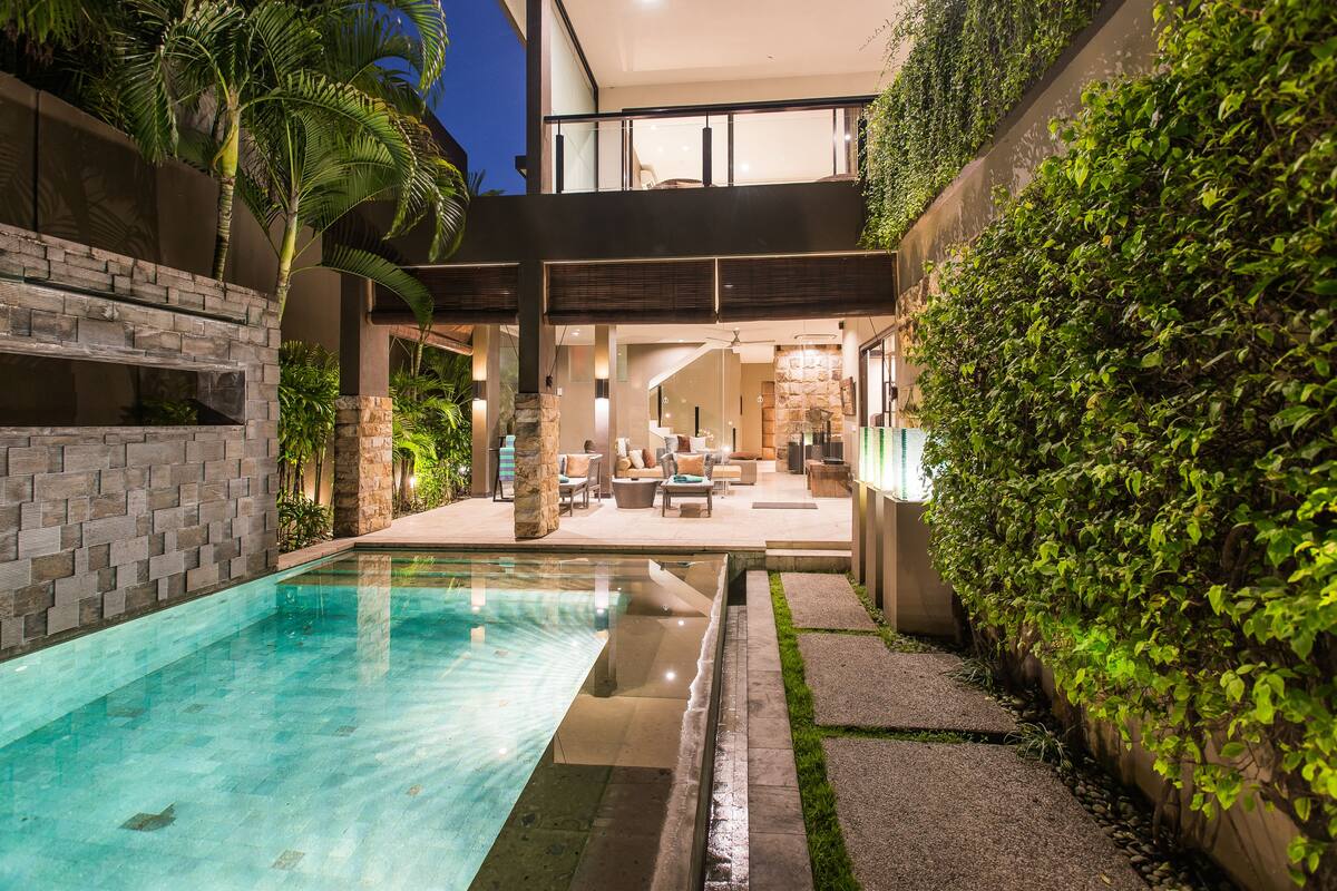 A modern outdoor pool area with a stone wall and lush greenery.