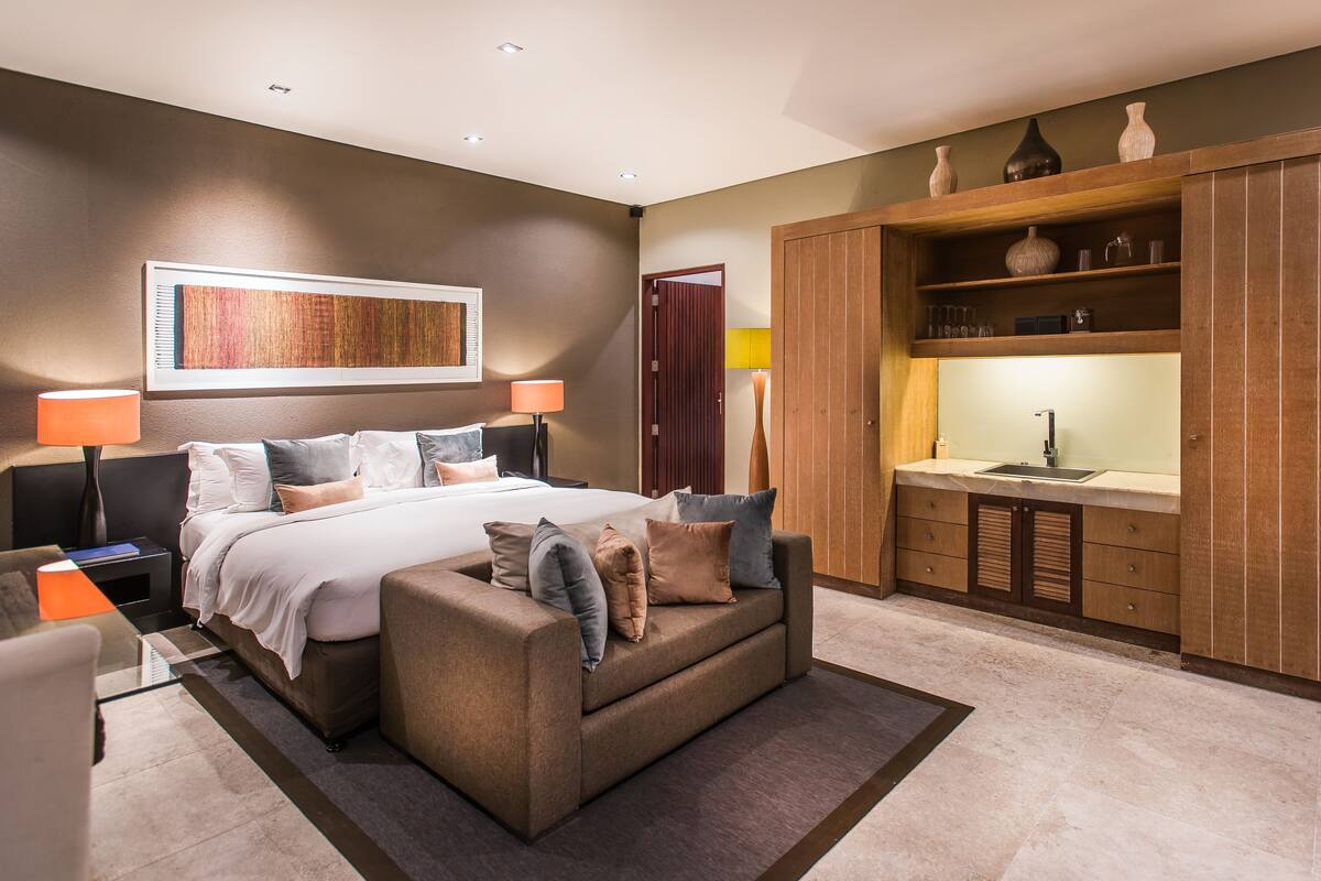 A modern bedroom with a large bed, a sofa, a desk, and a built-in wardrobe.