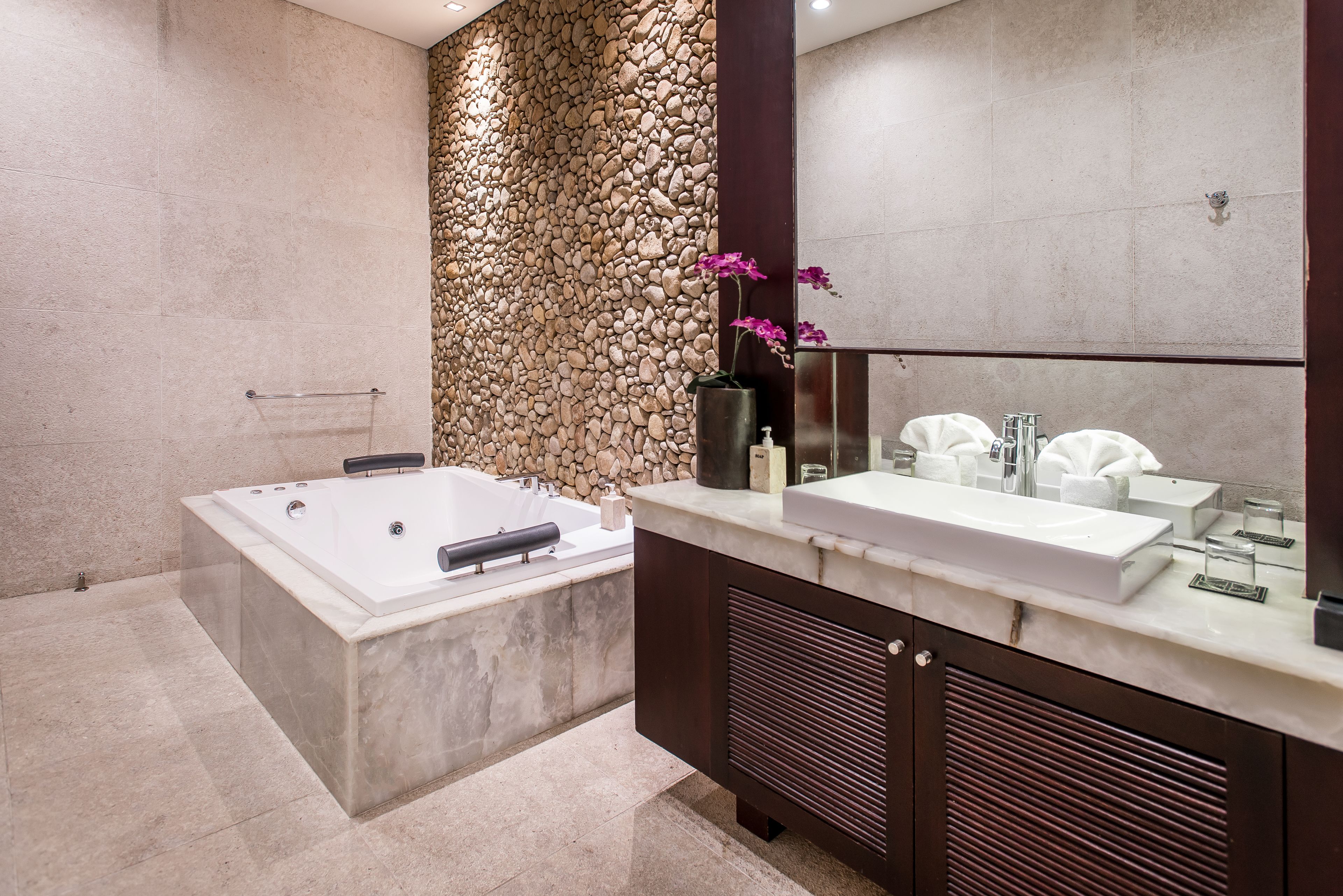 A modern bathroom with a stone wall, a large bathtub, and a vanity with a mirror.