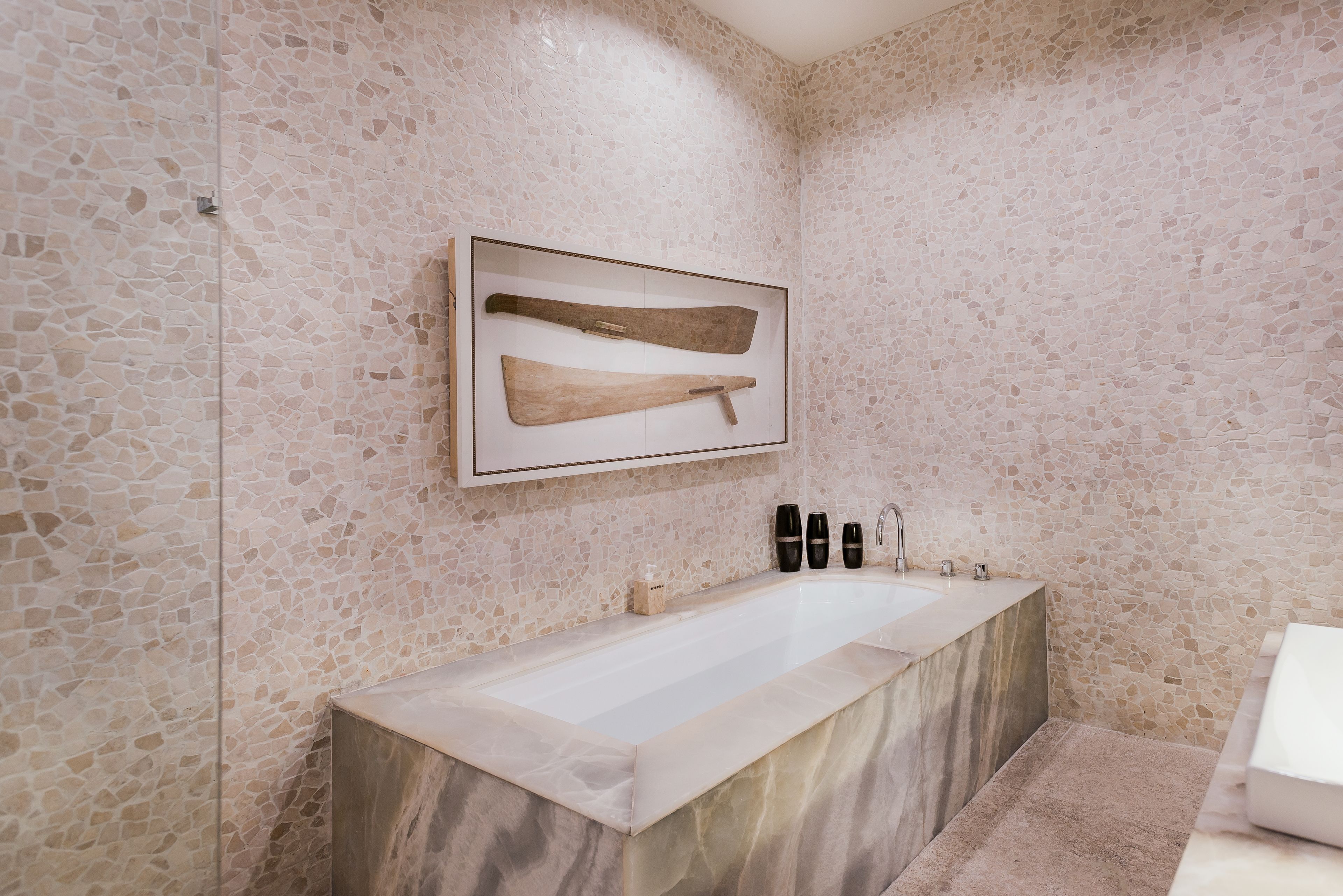 A modern bathroom with a large marble sink, a framed picture of wooden tools, and a small shelf with toiletries.