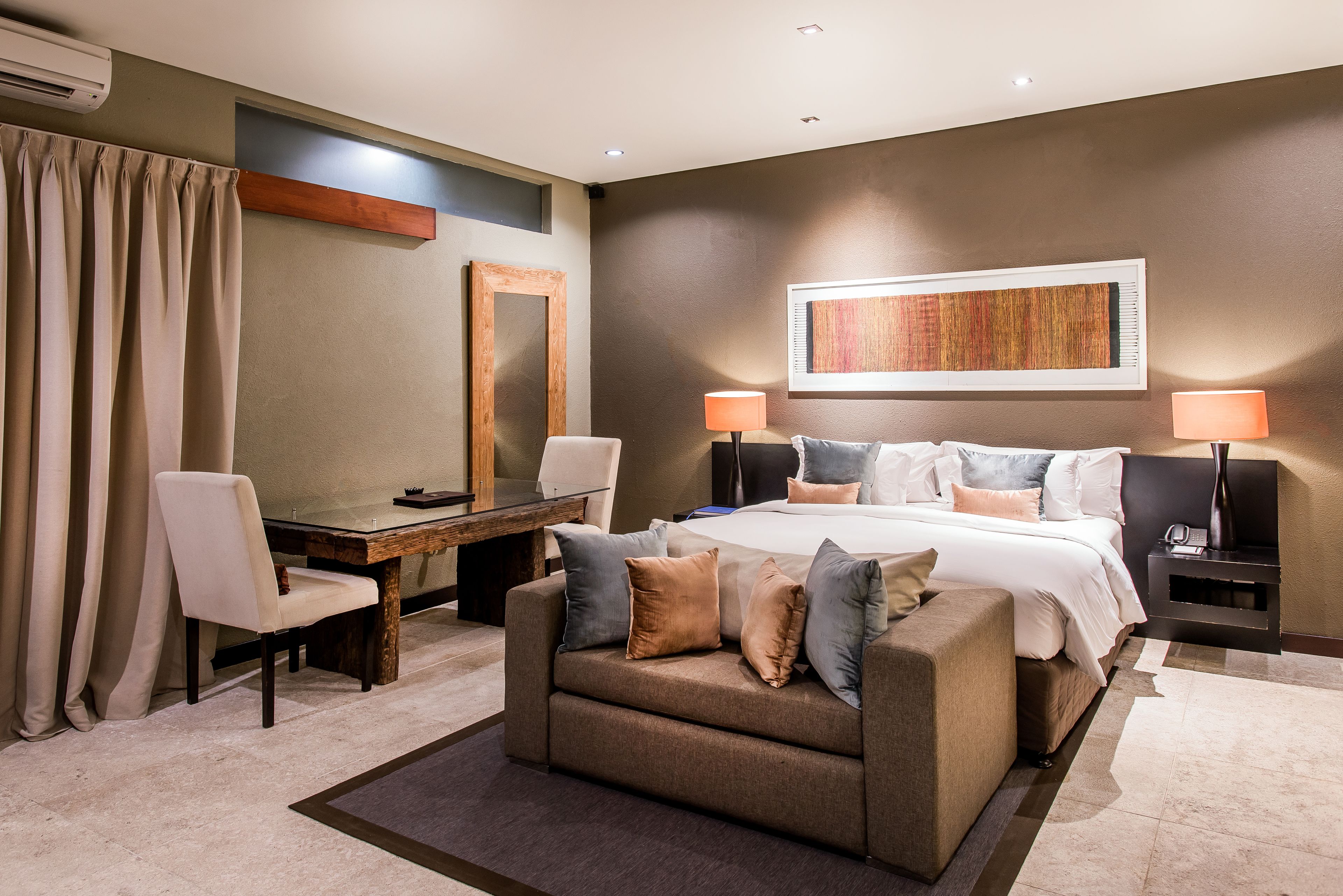 A modern hotel room with a bed, a desk, a chair, and a sofa.