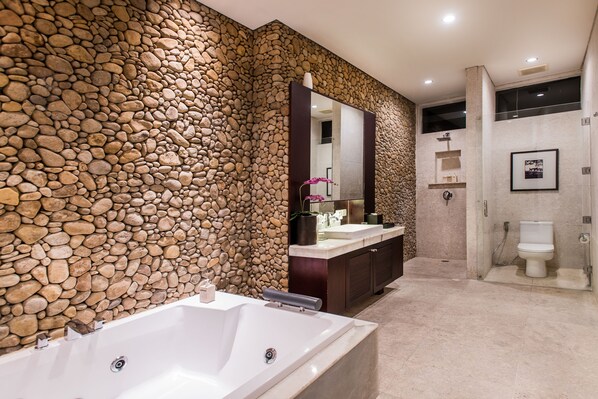A modern bathroom with a stone wall, a large bathtub, a vanity with a mirror, and a toilet.