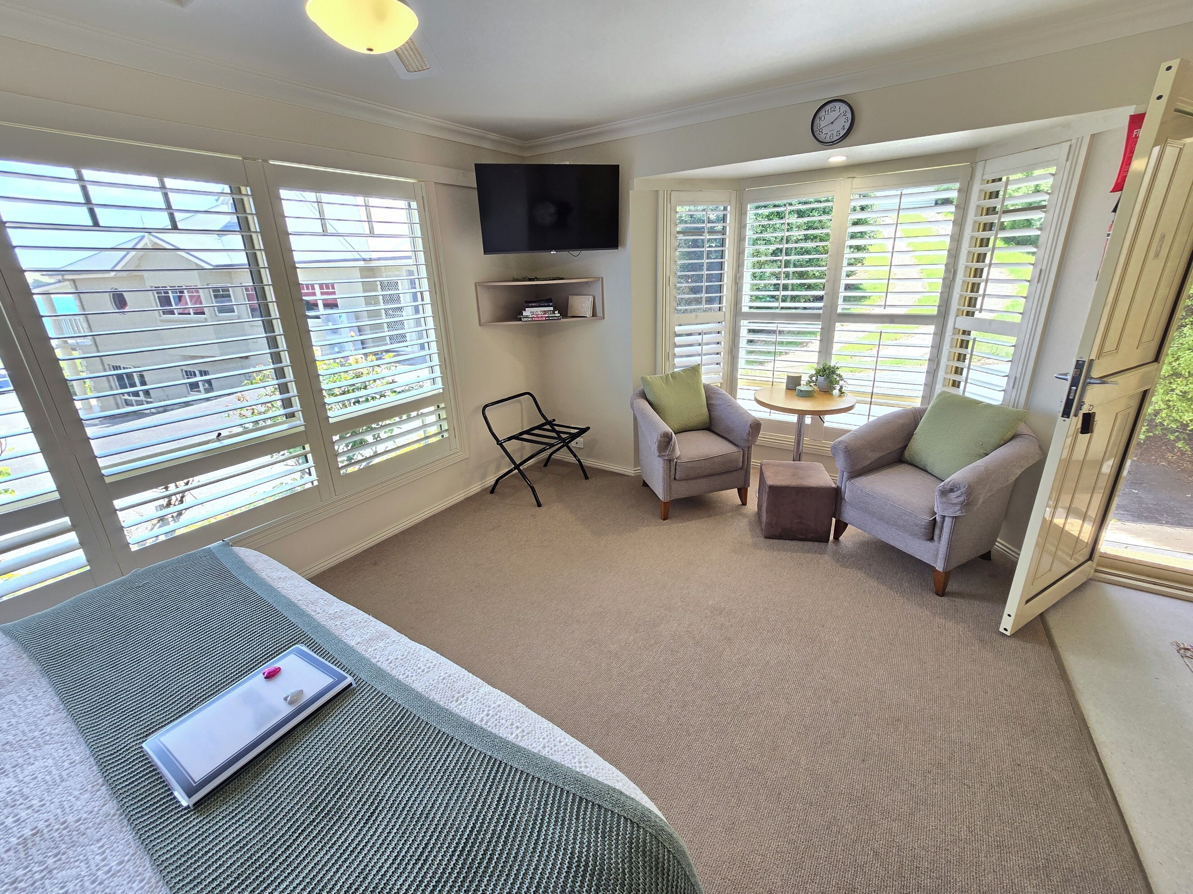 A cozy room with two armchairs, a small table, a flat-screen TV, and large windows with blinds.