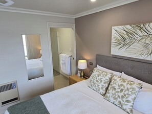 A hotel room with a bed, a nightstand, a lamp, a mirror, and a door leading to a bathroom. - On The Terrace Stanley (Stanley)