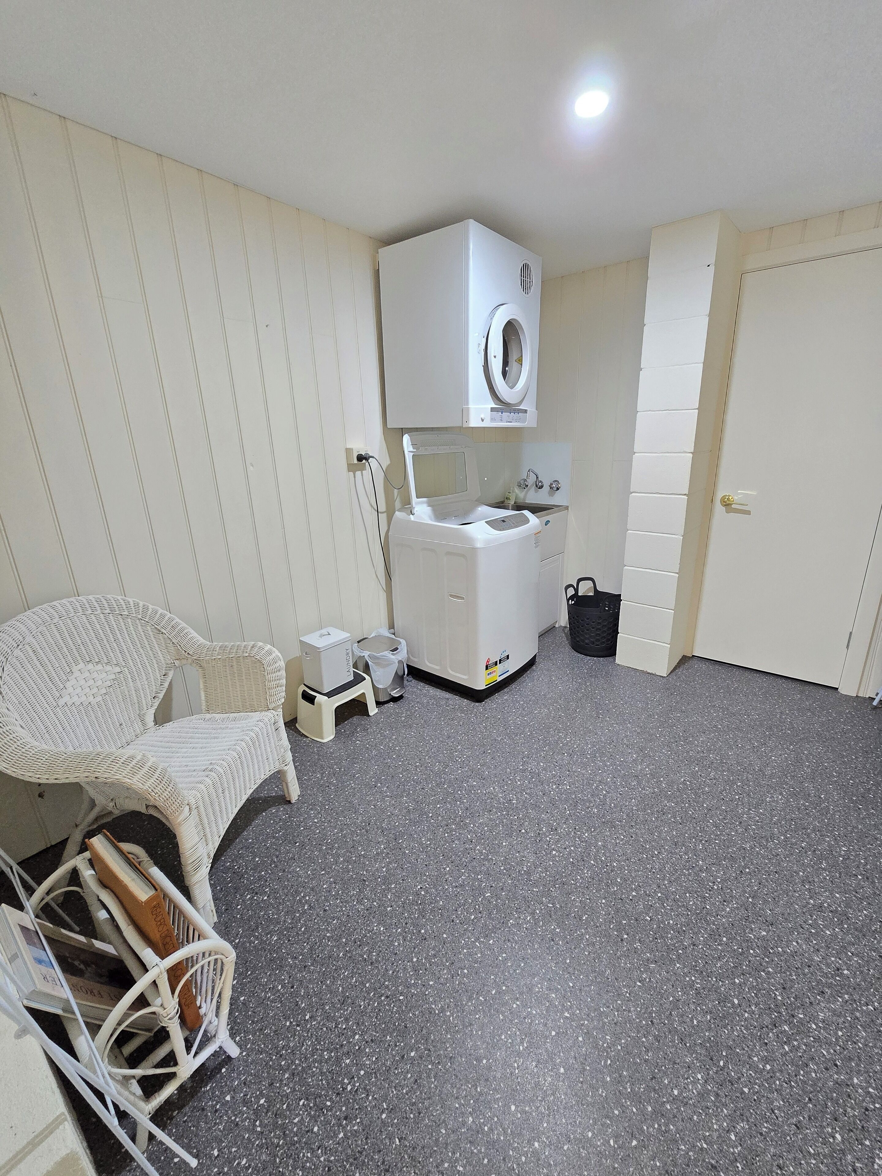 Habitación pequeña con lavadora, un taburete, una silla y una puerta.