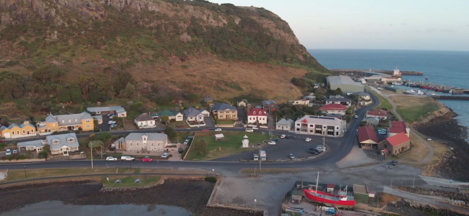Vista aérea de uma vila costeira com casas, uma estrada e um cais com um barco.