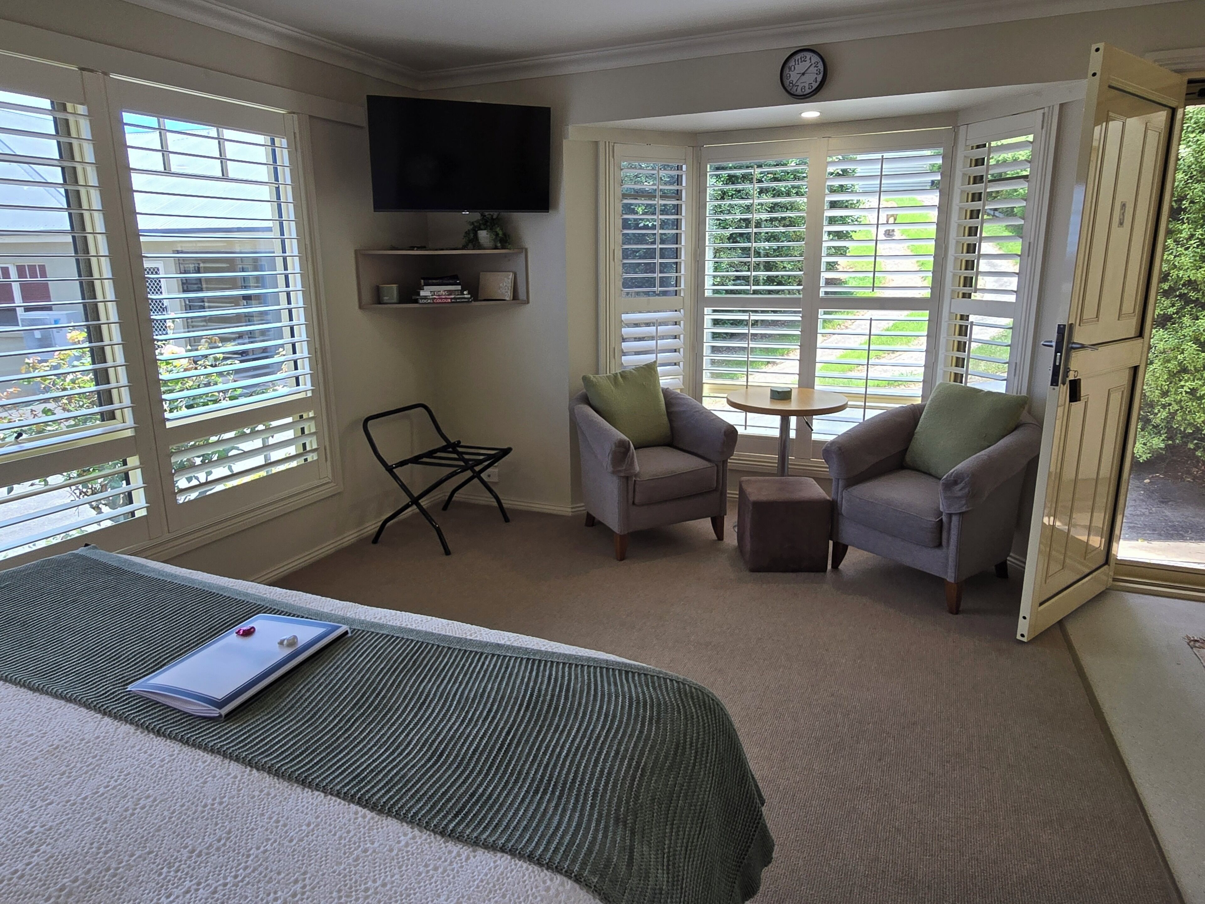 A hotel room with a bed, two armchairs, a small table, and a TV mounted on the wall.