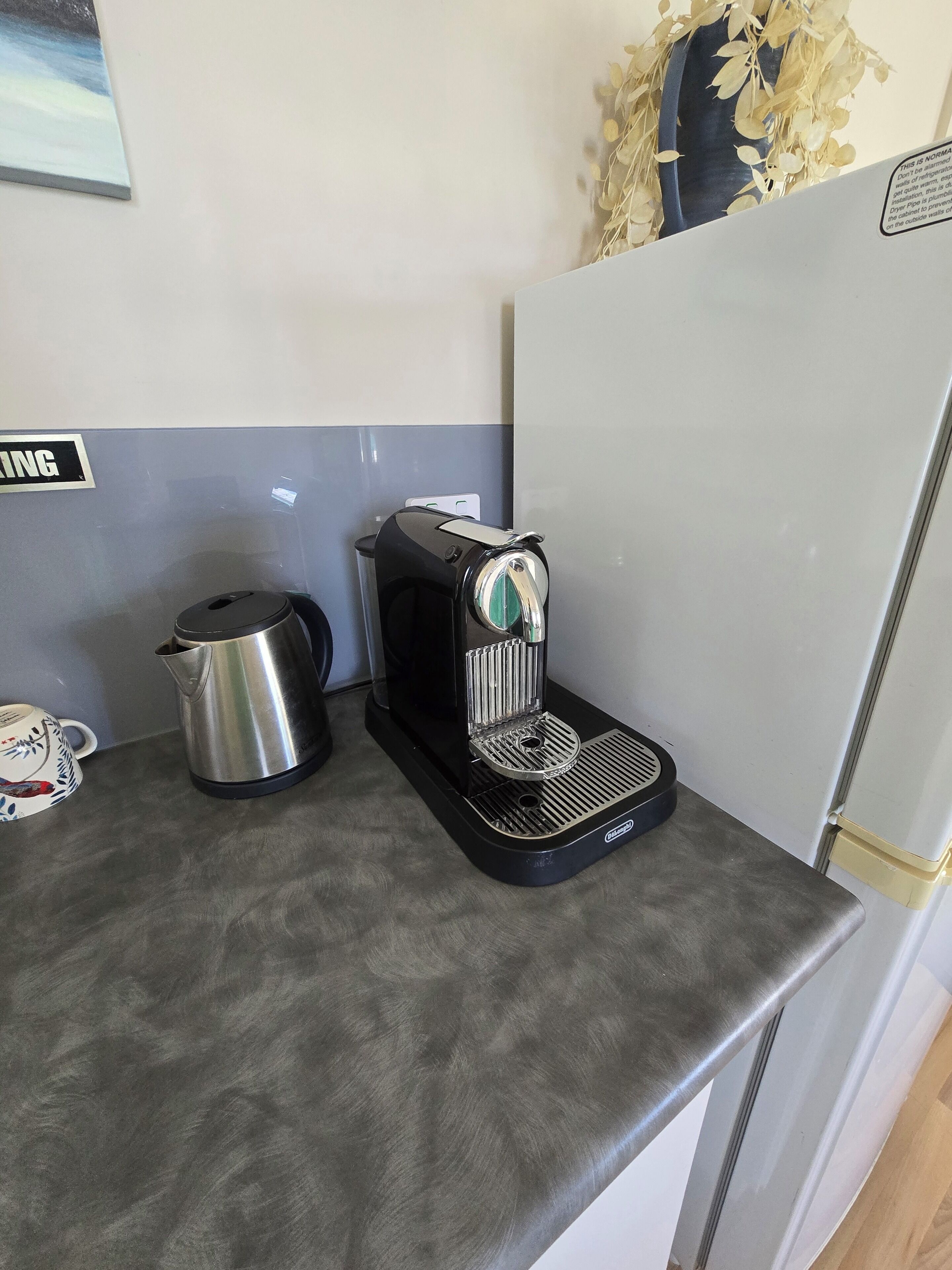 Une petite cuisine équipée d’une machine à café, d’une bouilloire et d’une tasse sur le plan de travail.