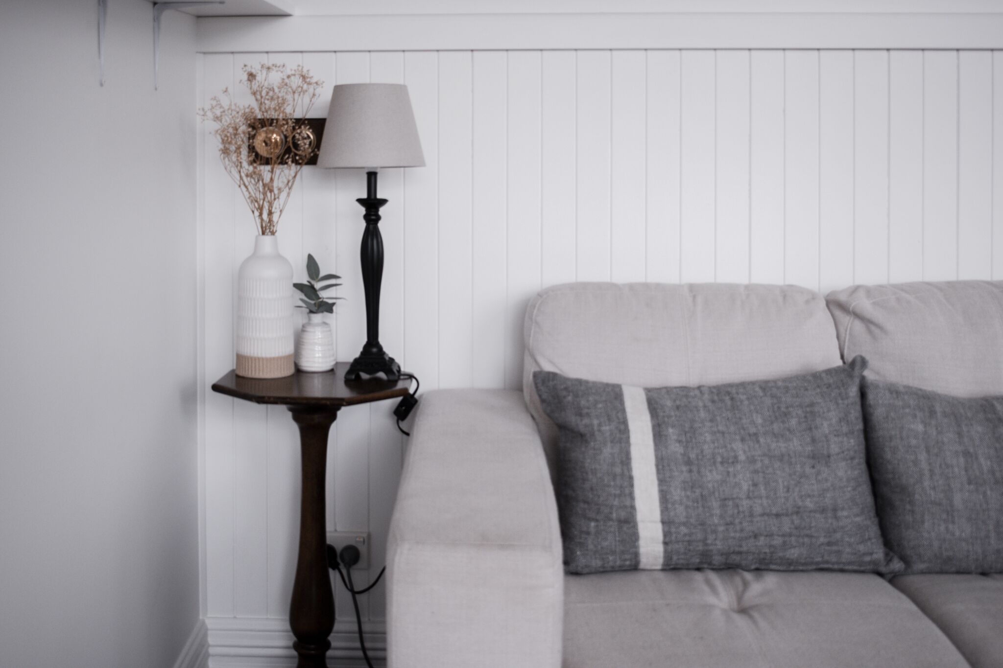 A modern living room with a grey sofa, a small side table with a lamp, and decorative items.