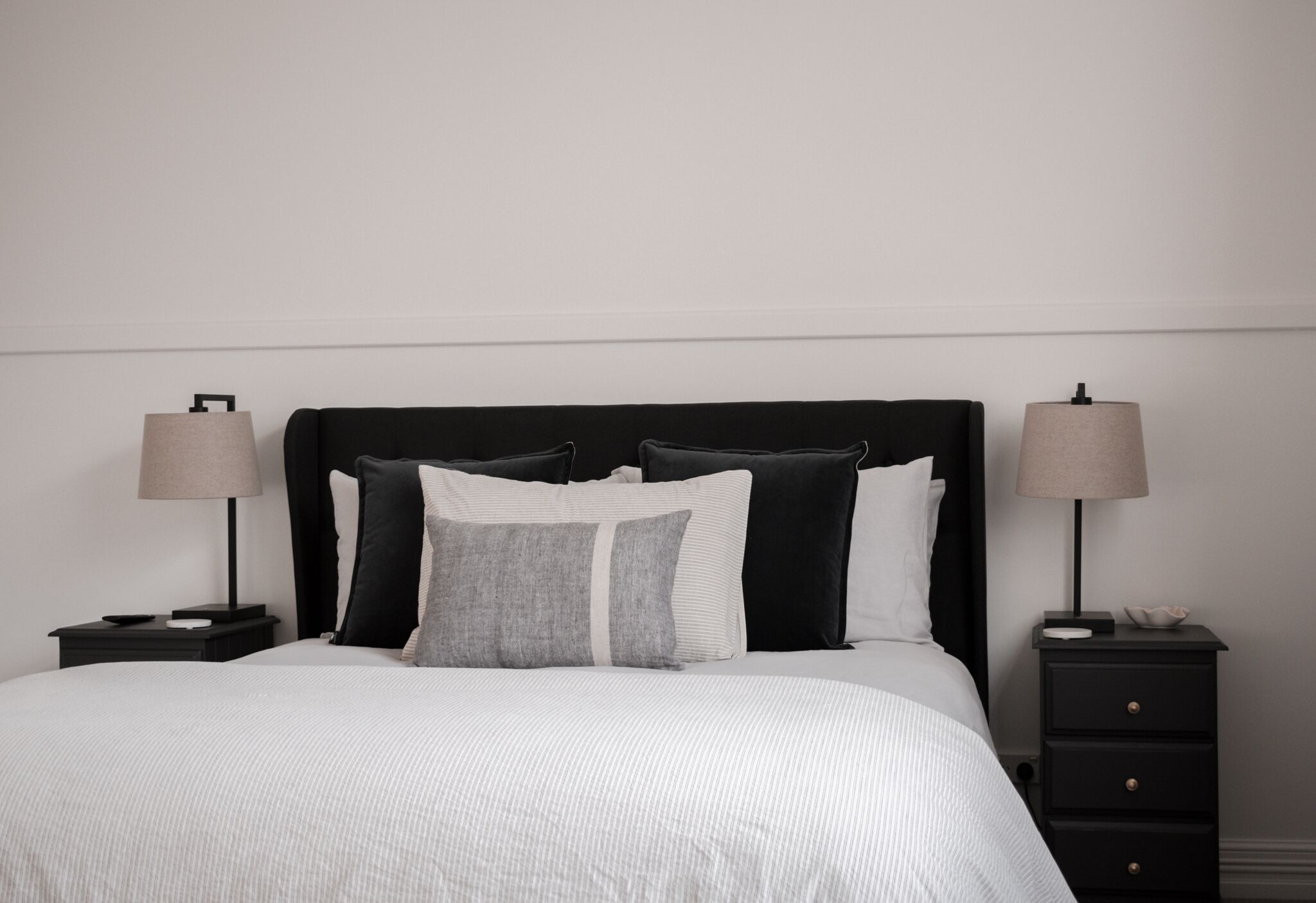 A neatly made bed with a white and gray striped duvet, two bedside tables with lamps, and a black nightstand with drawers.