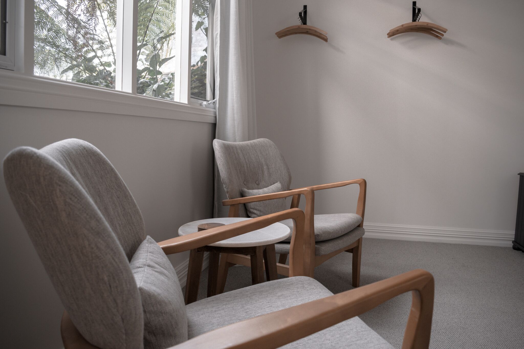A corner room with two grey upholstered chairs, a small round table, and a window with a view of trees.