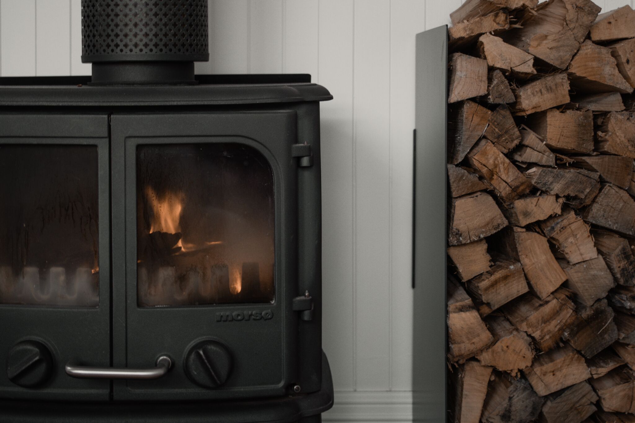 A wood-burning stove with a visible fire inside, next to a stack of firewood.