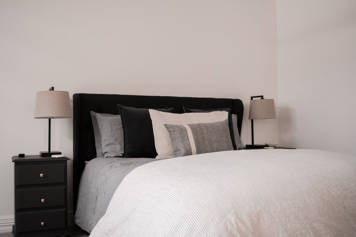 A bedroom with a black headboard, a white bedspread, and two bedside tables with lamps.