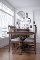 Comedor con mesa y sillas de madera, un espejo grande y una ventana con persianas.
