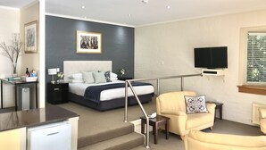 A modern hotel room with a bed, a desk, a chair, a TV, and a staircase. - Briars Country Lodge (Burradoo)