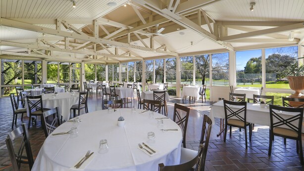 A covered outdoor dining area with round tables and chairs, large windows, and a view of the outdoors. - Briars Country Lodge (Burradoo)
