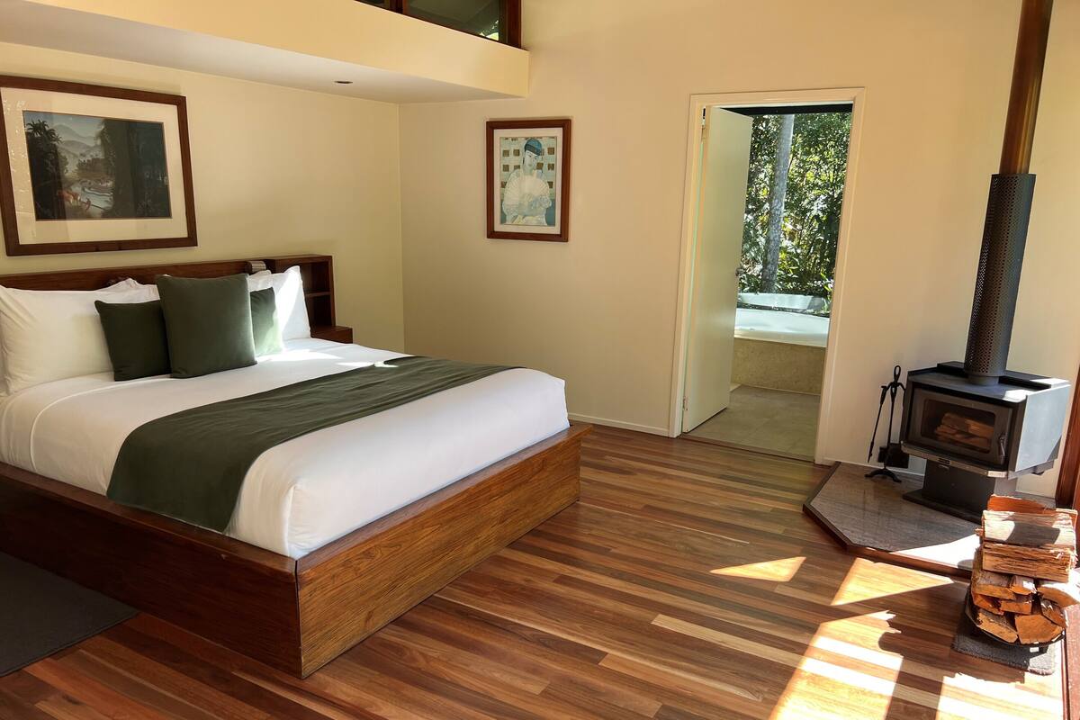 Une chambre avec un lit en bois, une grande fenêtre et un poêle à bois.