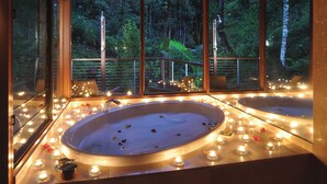 A spa area with two hot tubs surrounded by candles and a view of a forest through large windows. - Crystal Creek Rainforest Retreat (Upper Crystal Creek)