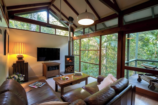 A spacious living room with a large window, a fireplace, a sofa, and a coffee table. - Crystal Creek Rainforest Retreat (Upper Crystal Creek)
