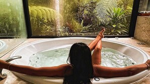 A person relaxing in a bathtub with a view of a forest through a large window. - Crystal Creek Rainforest Retreat (Upper Crystal Creek)