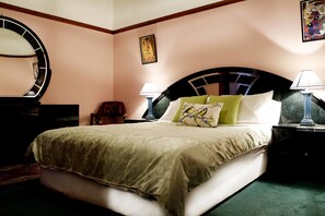 A neatly made bed with a green and white duvet, two bedside lamps, a round mirror, and a framed painting on the wall. - Apartments Downtown (Burnie)