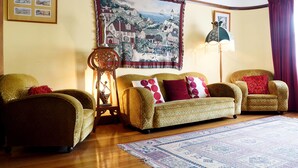 A living room with a patterned sofa, a wooden side table, a floor lamp, and a large tapestry on the wall. - Apartments Downtown (Burnie)