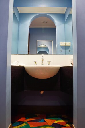A bathroom with a white sink, blue walls, a mirror, and a colorful floor. - Apartments Downtown (Burnie)