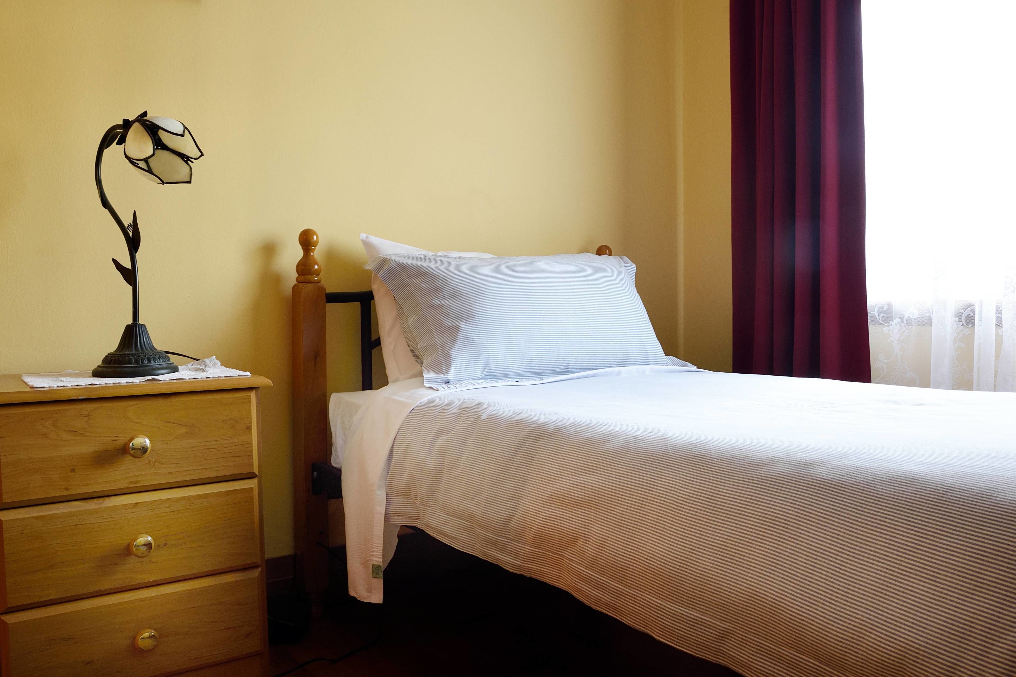 Una cama bien hecha con una colcha a rayas, una almohada blanca y una mesita de noche de madera con cajones.