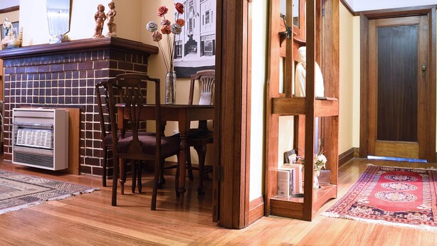 A cozy living room with a fireplace, wooden furniture, and a rug. - Apartments Downtown (Burnie)