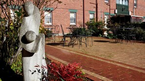 A courtyard with a stone sculpture, outdoor seating, and a brick building in the background. - Apartments Downtown (Burnie)