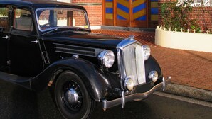 A vintage black car parked in front of a brick building with a sign reading "Apartments Down Town Accommodation". - Apartments Downtown (Burnie)