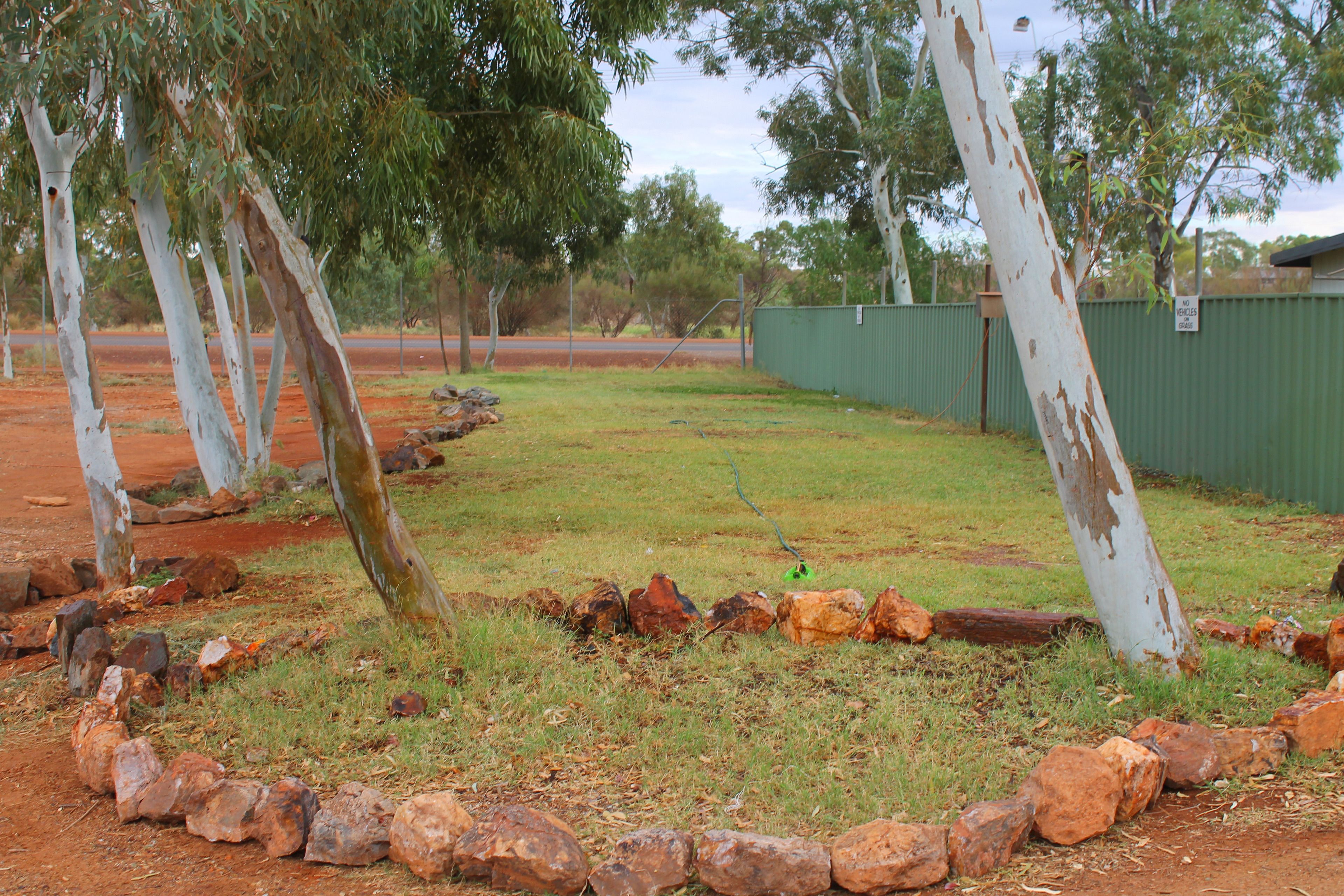 A grassy area with rocks, trees, and a green fence.