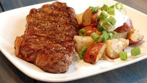 Ein Teller mit einem Steak, Bratkartoffeln und einer Marinade aus grünen Zwiebeln.