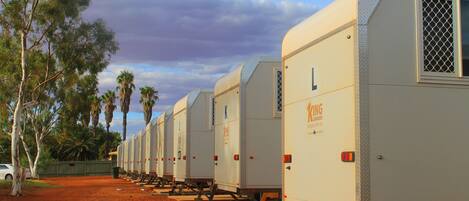 A row of mobile homes with a dirt ground and trees in the background.