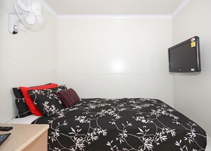 A small, neatly arranged bedroom with a bed, a TV mounted on the wall, a bedside table with a remote control, and a wall-mounted fan. - Meekatharra Accommodation Centre - Campsite (Meekatharra)