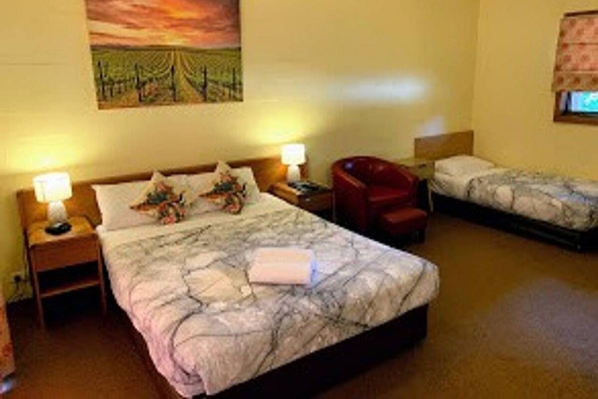 A hotel room with a large bed, a smaller bed, a chair, and a painting on the wall.