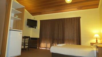 Una habitación de hotel con una cama, un escritorio con silla, un televisor montado en la pared y una ventana con cortinas.