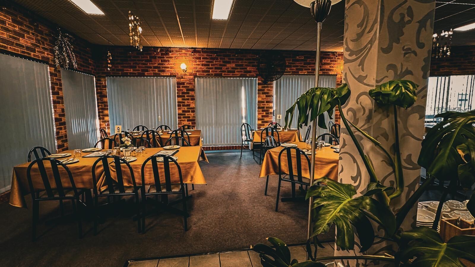 A dining area with brick walls, large windows with blinds, and tables set for dining.