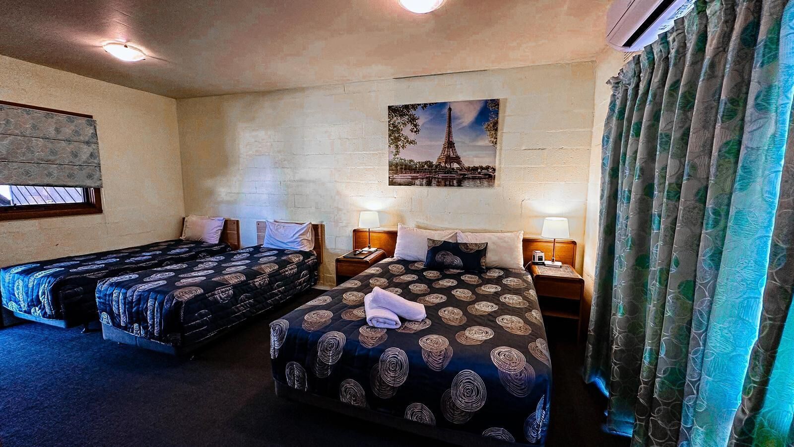 Une chambre d’hôtel avec deux lits, un tableau représentant la Tour Eiffel et une fenêtre avec des rideaux.
