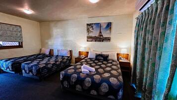 Une chambre d’hôtel avec deux lits, un tableau représentant la Tour Eiffel et une fenêtre avec des rideaux.