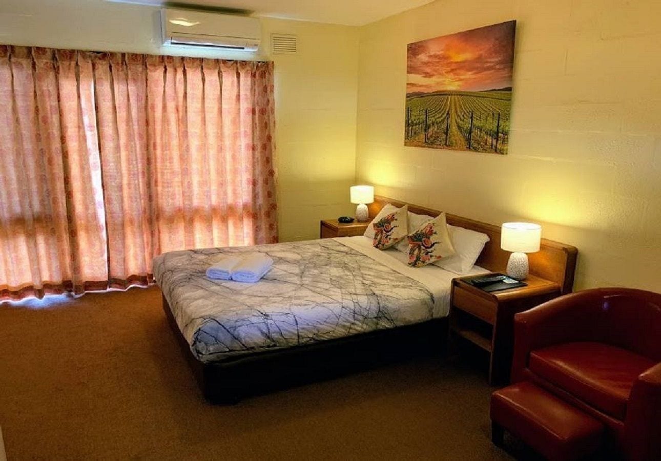 Une chambre d’hôtel avec un lit, deux tables de chevet, une chaise rouge et un tableau au mur.