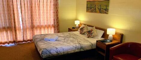 Une chambre d’hôtel avec un lit, deux tables de chevet, une chaise rouge et un tableau au mur.