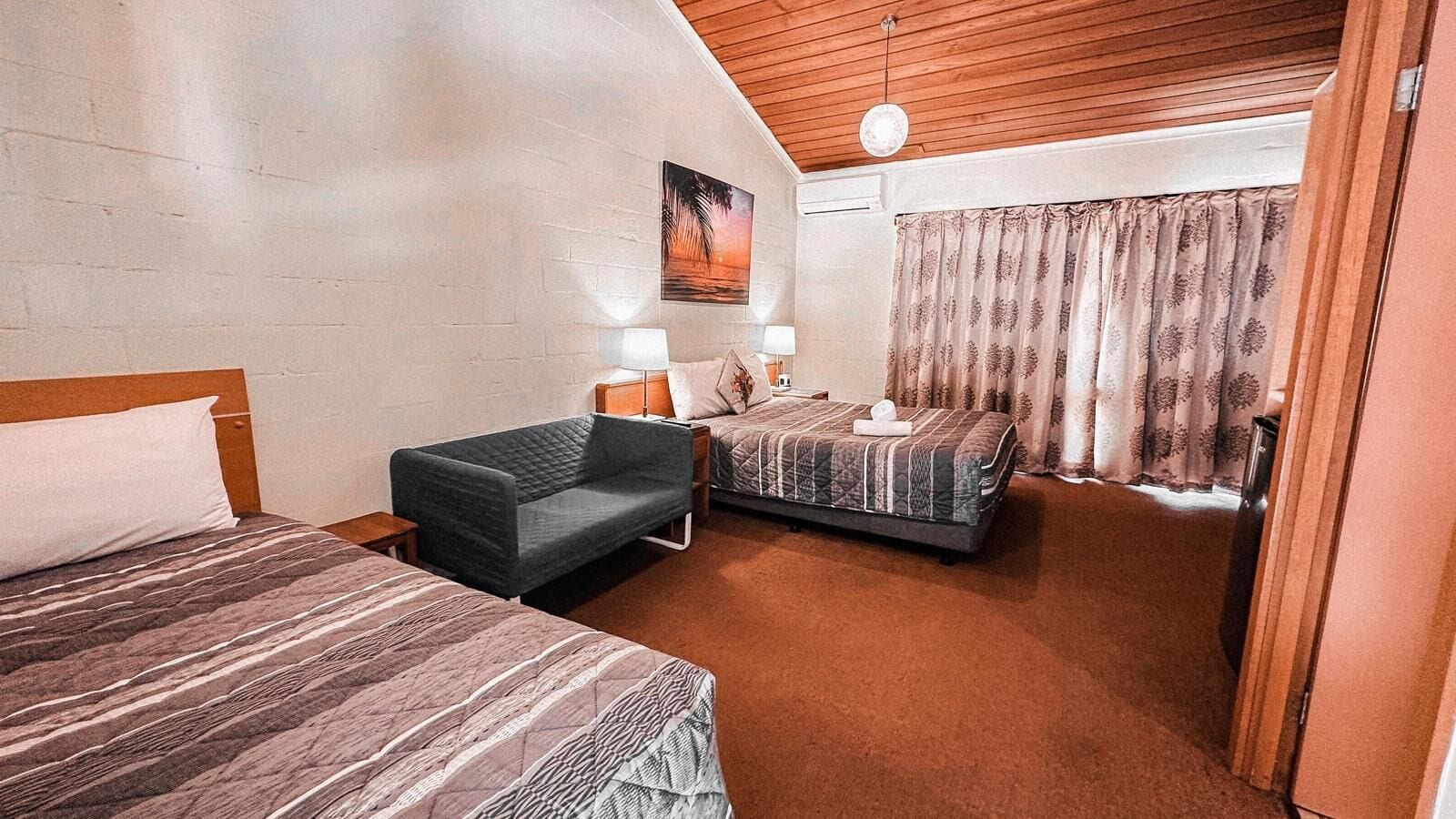 A room with two beds, a sofa, a painting on the wall, and a window with curtains.