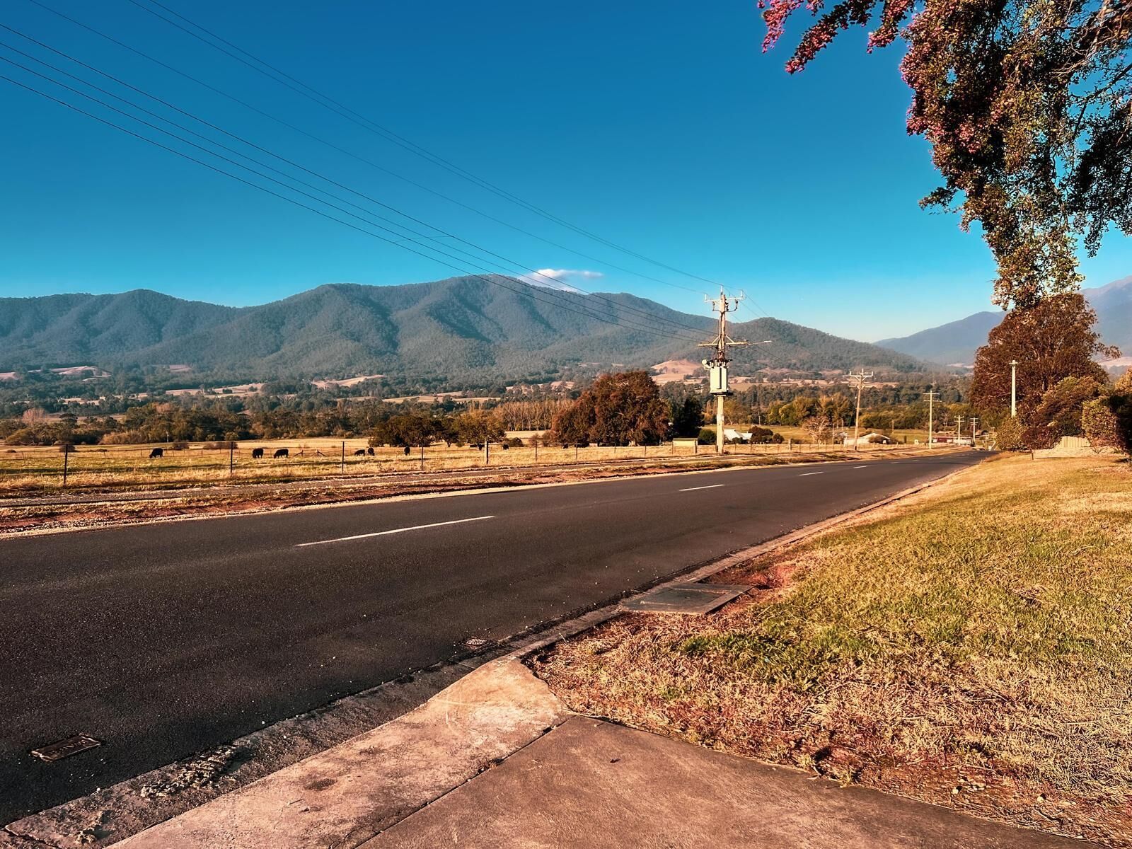 Una carretera con acera, un poste de luz y una cadena montañosa al fondo.