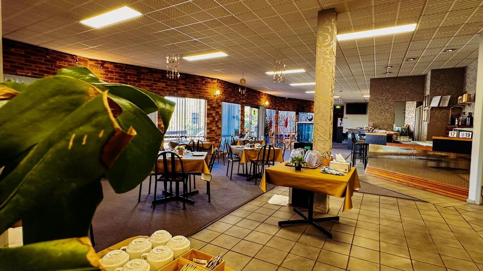 A restaurant with multiple tables and chairs, a brick wall, and a tiled floor.