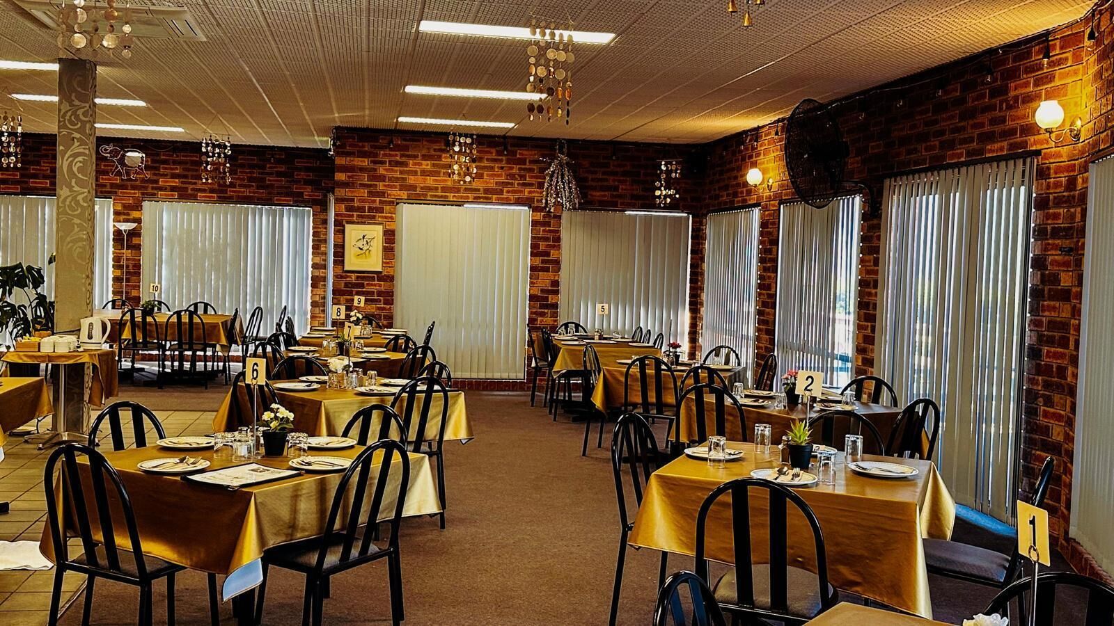 Un restaurante con varias mesas, cada una con un número, frente a paredes de ladrillo y amplias ventanas con persianas.