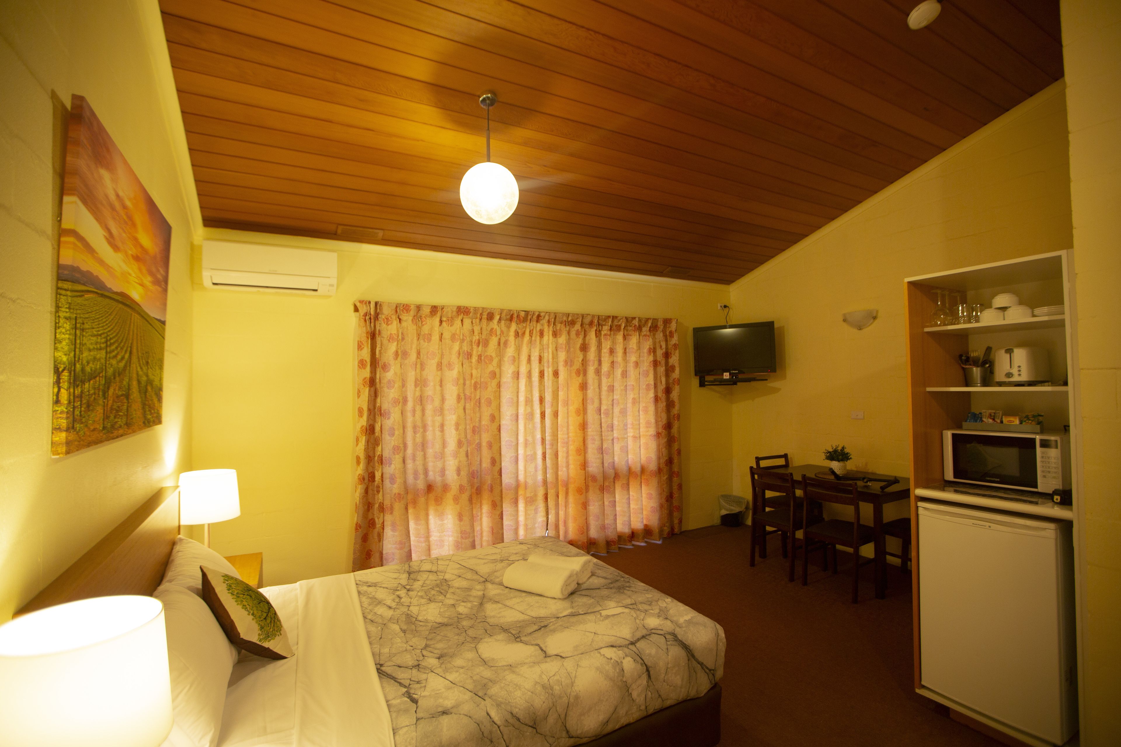 Una habitación de hotel con cama, escritorio, silla, televisor y refrigerador.