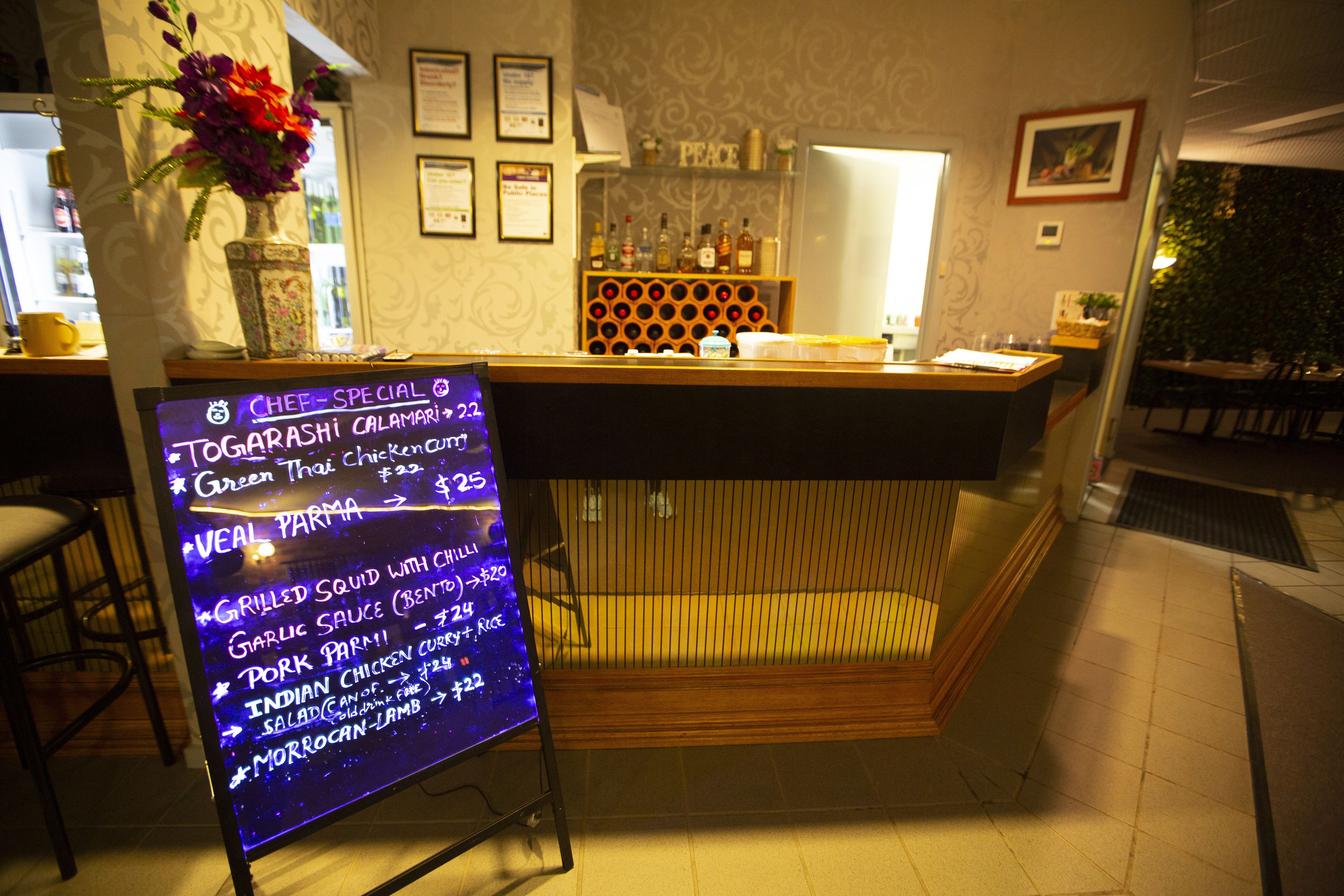 A restaurant interior with a menu board, wooden counter, and a wall with framed certificates.