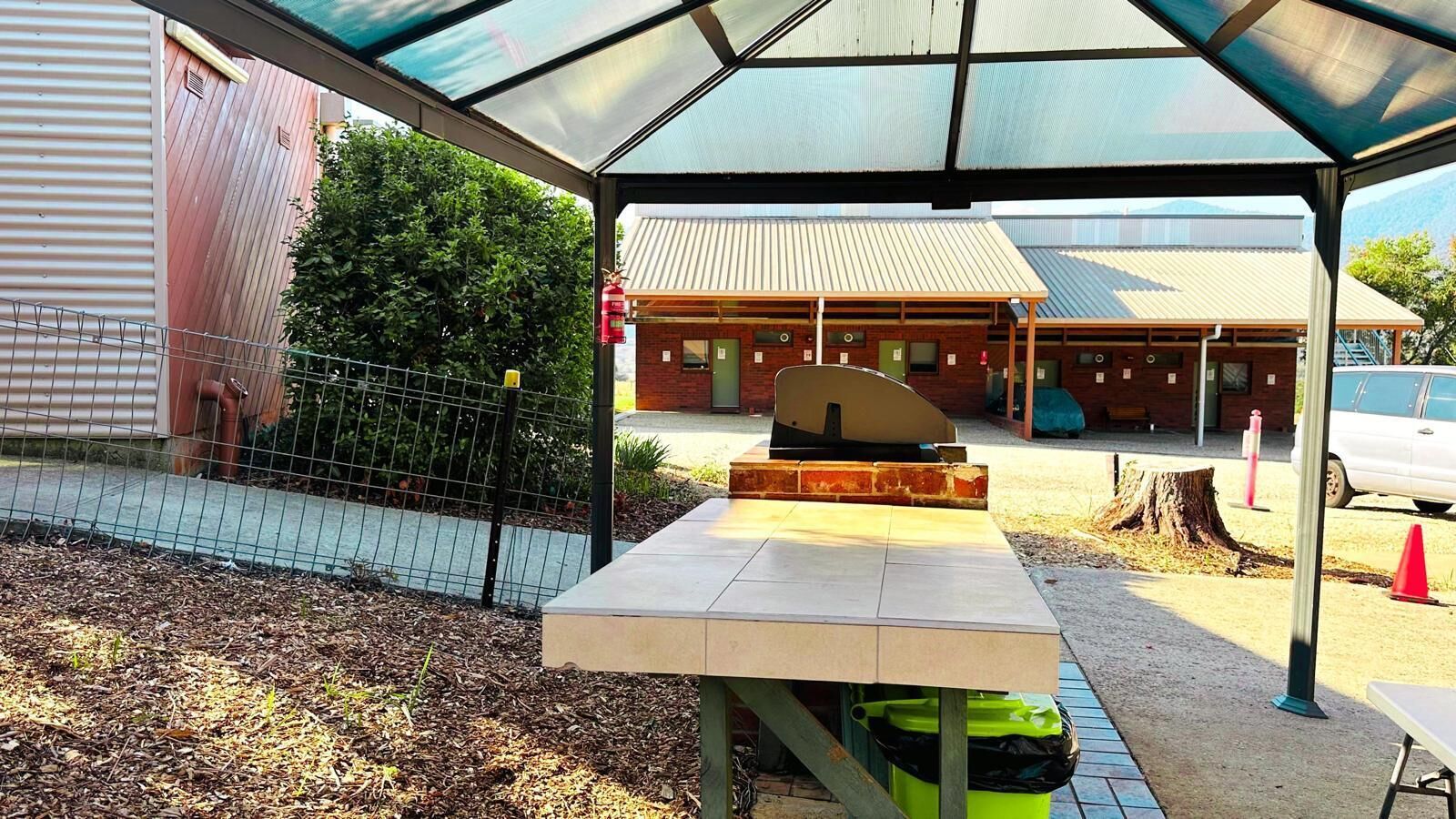 An outdoor seating area with a table and chairs, a covered structure, and a building in the background.